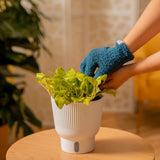 A Nen Joy pothos plant is tended by a person. Their hand extends out to clean the leaves of the plant, and they are wearing blue fuzzy gloves. The plant sits on a small light-woodedn table with a blurred backdrop. 